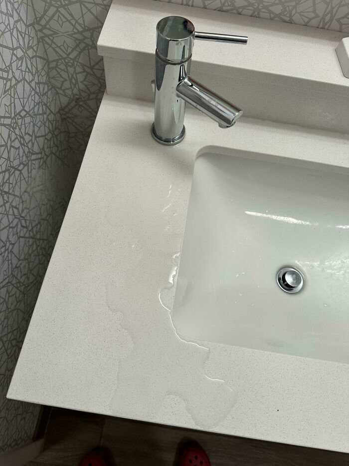 Water pooling on a bathroom sink countertop due to a poor designer decision creating avoidable problems.
