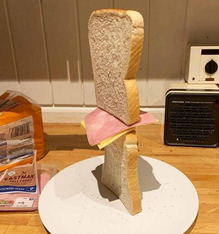 A random and cringe photo of an unbalanced sandwich with slices of bread, ham, and cheese stacked vertically on a plate.