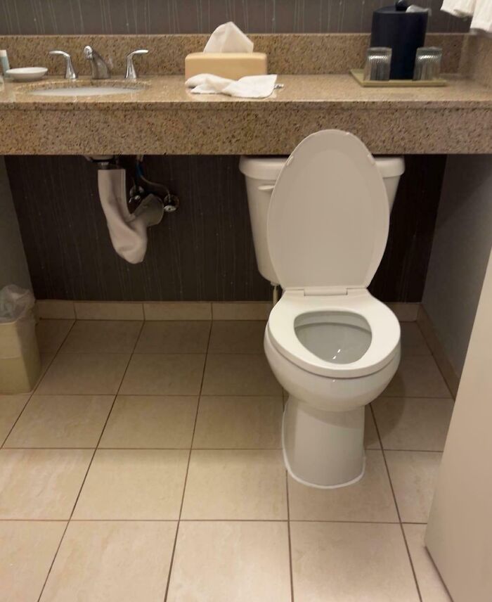 Bathroom with a toilet placed awkwardly close to the sink counter highlighting dumb designer decisions causing issues.