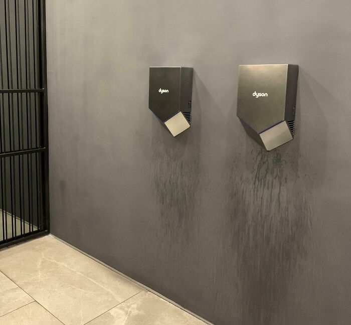 Hand dryers on a gray wall showing poor design with water stains underneath, illustrating dumb design decisions.