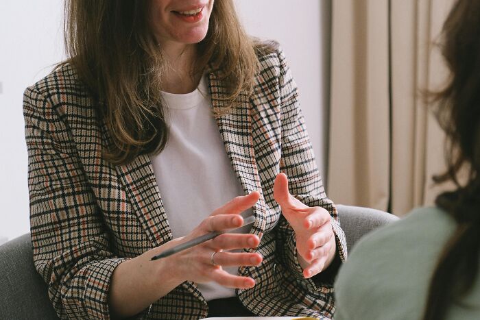 A woman in a plaid blazer talking and gesturing while discussing difficult coworkers in an office setting.