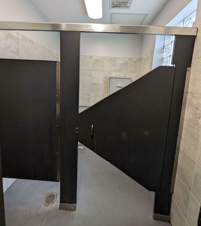Bathroom stall with a poorly designed door creating awkward problems, showcasing designers' dumb decisions and design flaws.