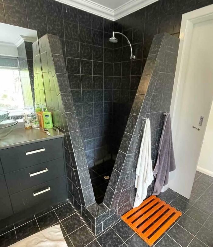 Awkwardly designed shower with angled black tiles and towels hanging on the outside, showing dumb design decisions.