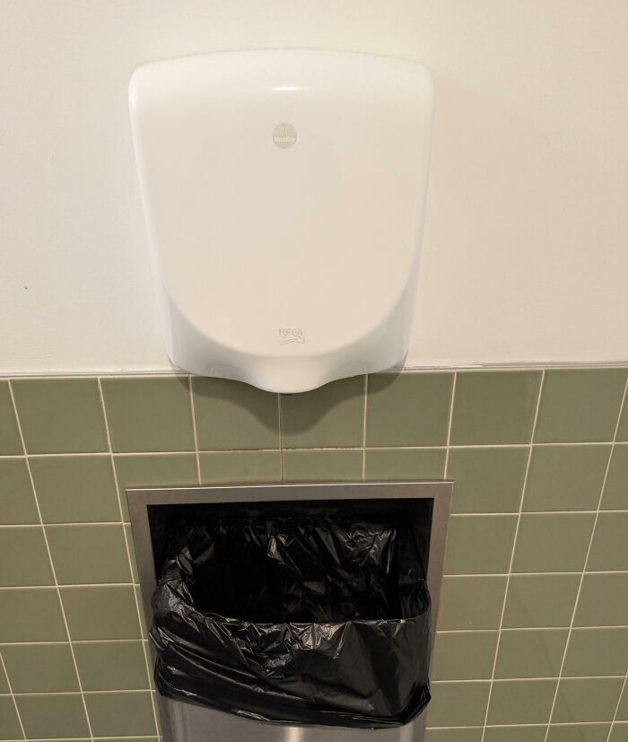 Hand dryer placed directly above trash can, illustrating poor design choice creating problems nobody asked for.