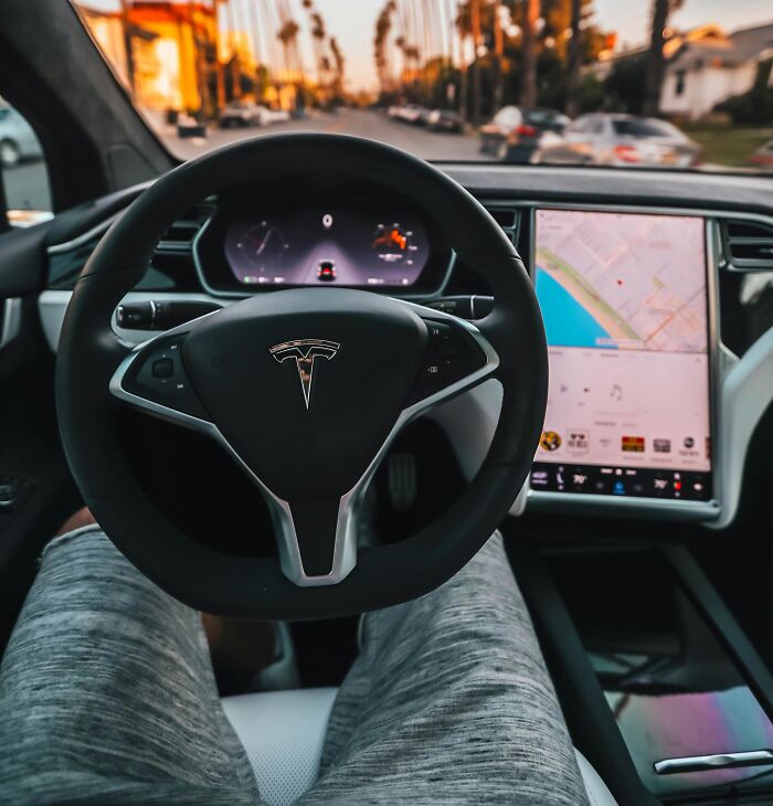 Tesla steering wheel and digital dashboard inside a luxury car, illustrating rich people lifestyle and out of pocket comments.