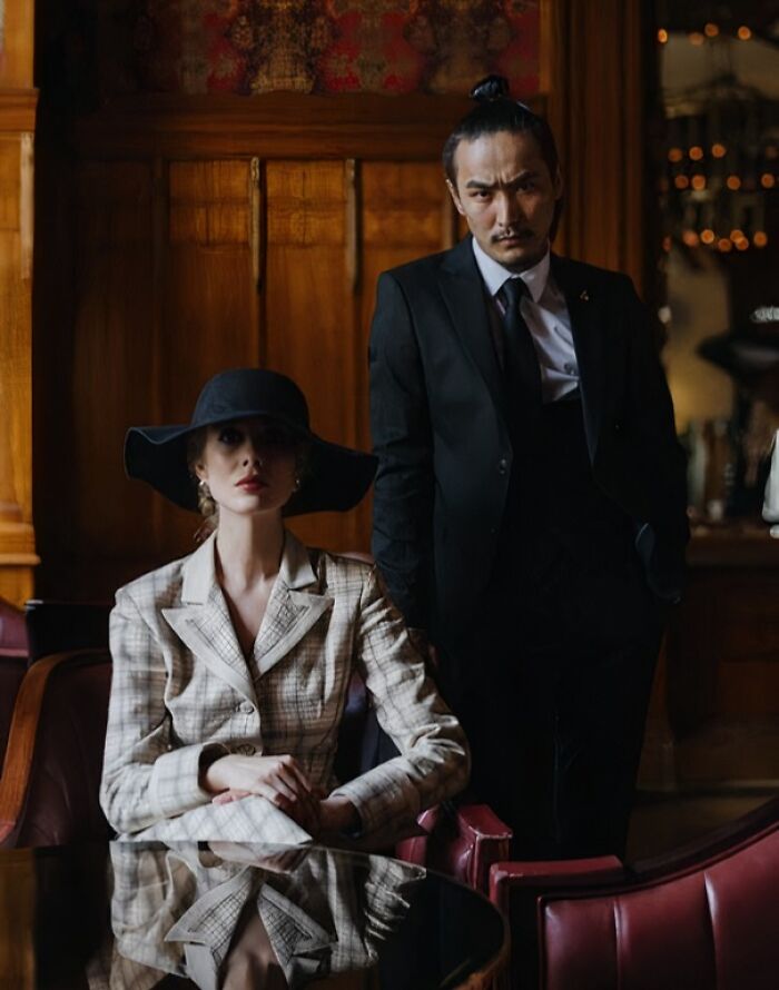 Two stylish people in formal attire posing indoors, representing themes of family secrets and personal stories.