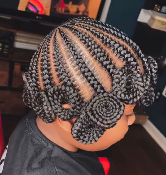 Child with intricate braided hairstyle featuring spiral designs and neat cornrow sections in an indoor setting.