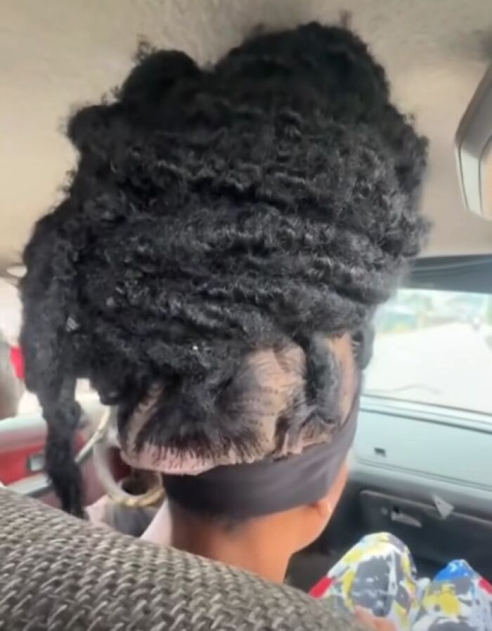 Disastrous hairstyle featuring thick, uneven twisted hair piled high on a person sitting inside a car.