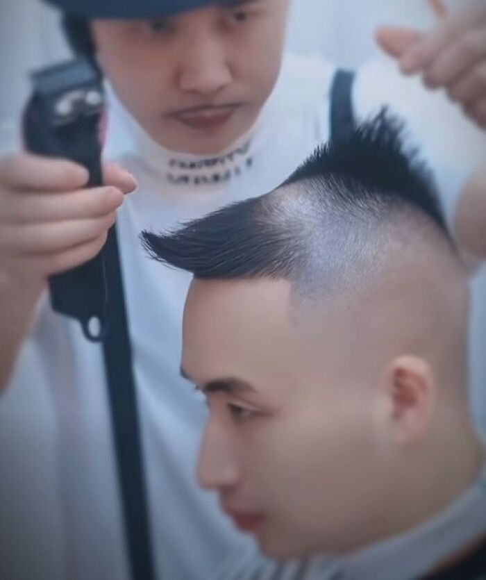 Barber creating a disastrous hairstyle with shaved sides and spiked top on a young man in a salon.