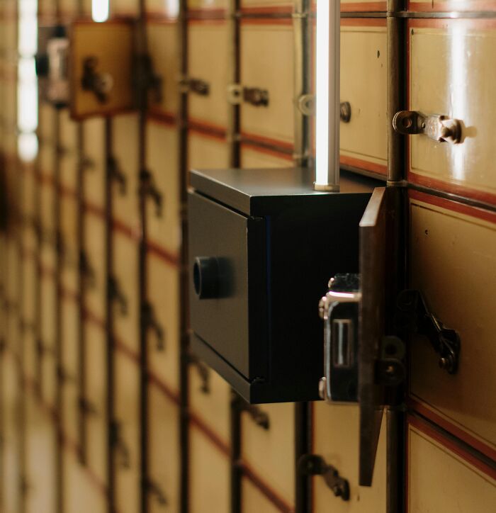 Open black safe deposit box among rows of old metal safety deposit boxes in a secure bank vault.