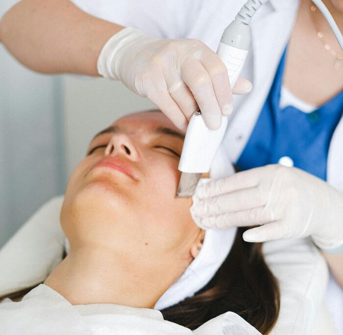 Person receiving a facial treatment from a professional wearing gloves and using a skincare device at a clinic.
