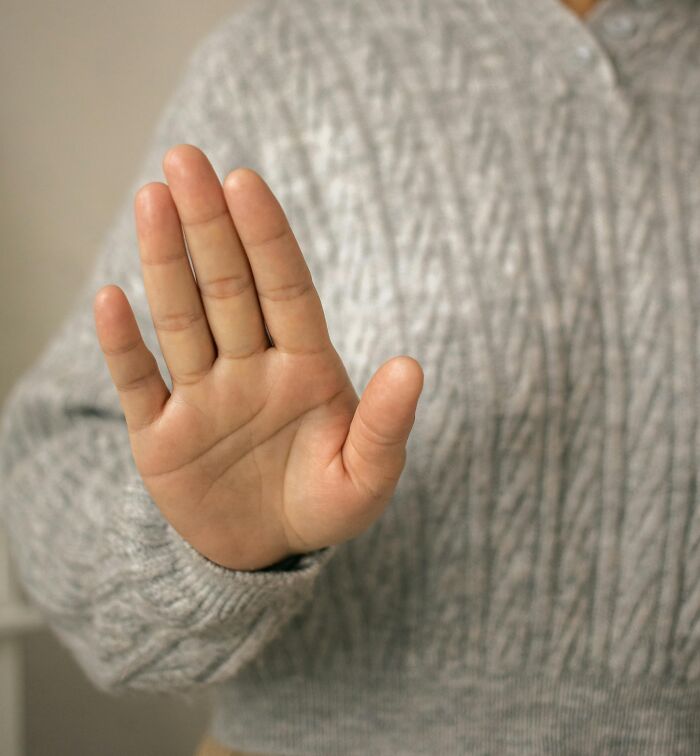 Hand raised in stop gesture, person wearing gray cable knit sweater, symbolizing rich people out of pocket statements.