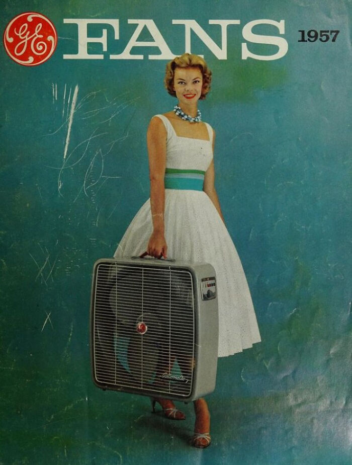 1957 vintage advertisement showing a woman in a white dress holding a large GE box fan against a blue background.