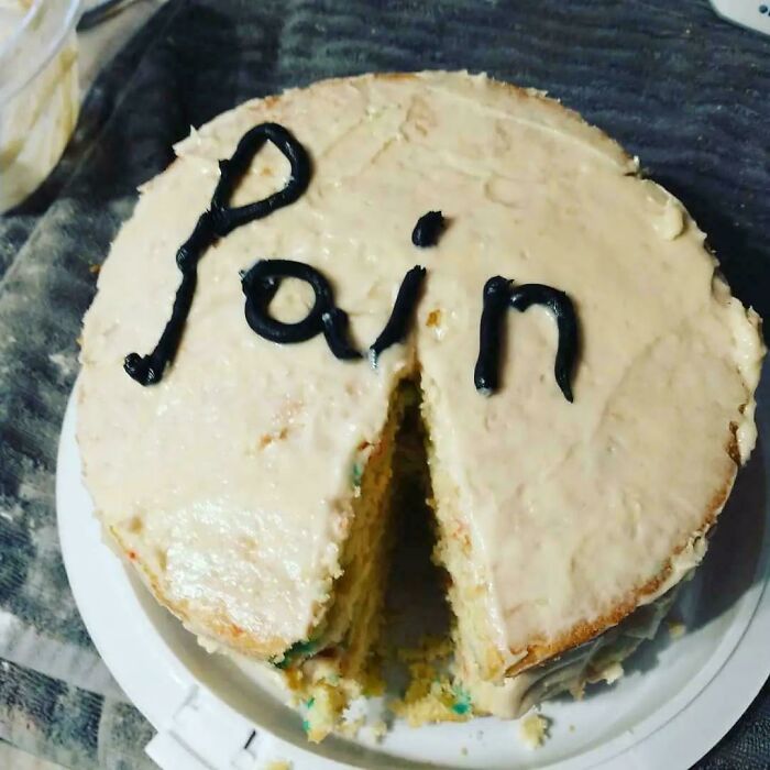 Cake with the word pain written in black icing, showing a slice missing, reflecting funny honest emotions cake.