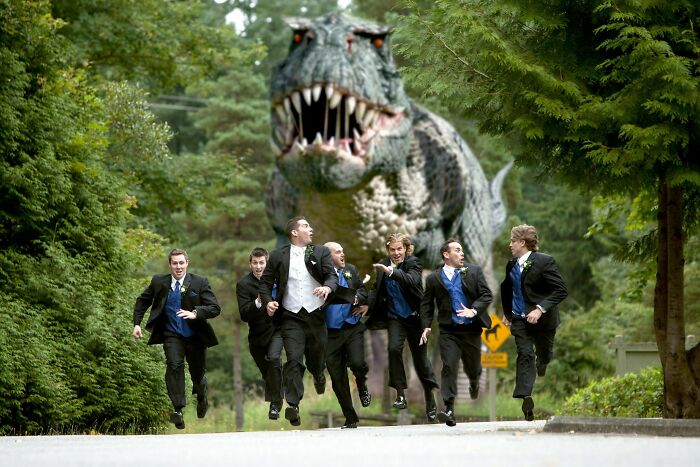 Group of groomsmen in suits running away from a large T-Rex, an awkward wedding photo with humorous effect.