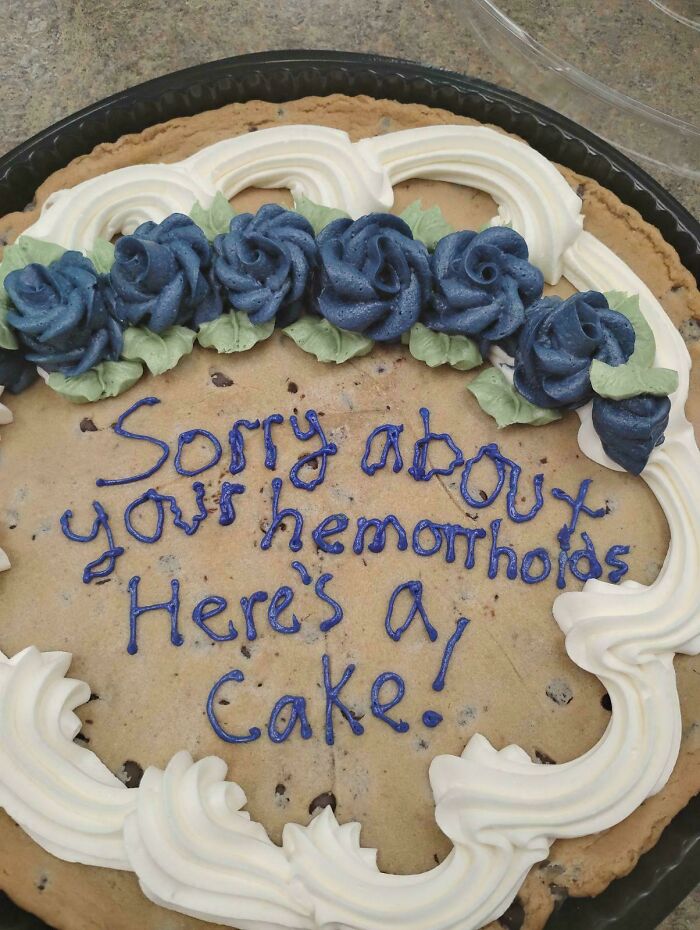 Large cookie cake with blue and white frosting flowers and a humorous, imperfectly written message in blue icing.