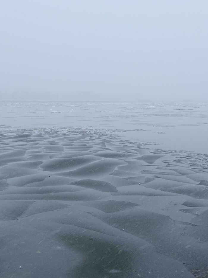 Frozen winter lake with smooth icy patterns under a grey sky, showcasing cozy winter nature without stepping into the cold.