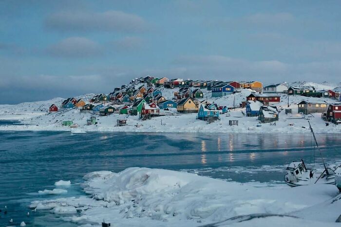 Colorful houses covered in snow along a frozen coastline creating cozy winter vibes without stepping into the cold.