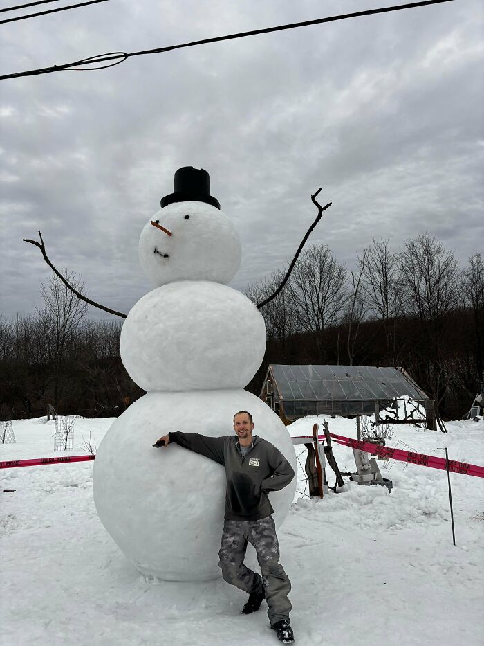 Man posing with a giant snowman in a snowy outdoor setting, showcasing cozy winter images without stepping into the cold.