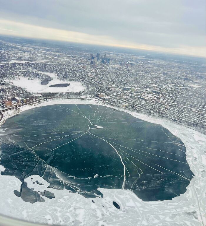 Aerial view of a frozen lake with cracks and snow-covered surroundings in winter, showcasing cozy winter scenery.