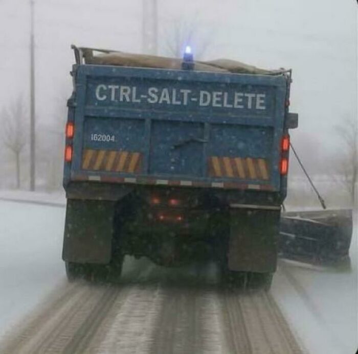Snow plow truck labeled CTRL-SALT-DELETE spreading salt on snowy road, showcasing cozy winter scenes without stepping into the cold.
