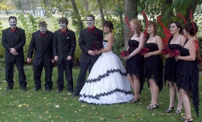 Bride and groom with groomsmen in skull makeup and bridesmaids in black dresses with red devil horns at an awkward wedding photo.