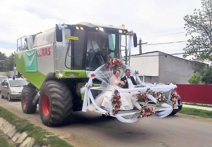 Bride and groom riding in a decorated combine harvester, creating an awkward wedding photo moment.