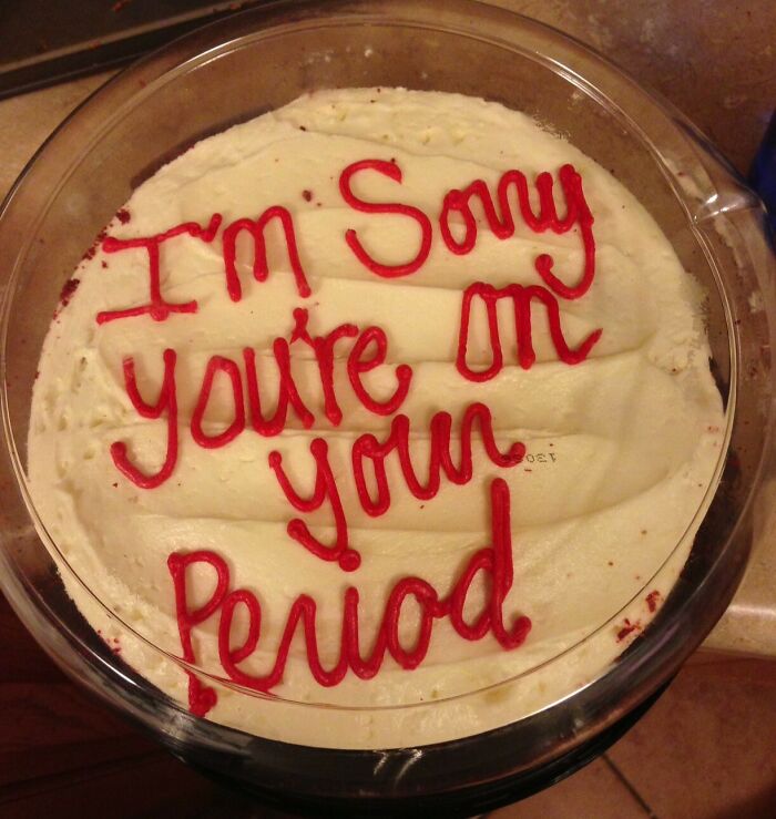 Funny cake with red icing text saying I'm sorry you're on your period, reflecting honest emotions on a white frosting base.