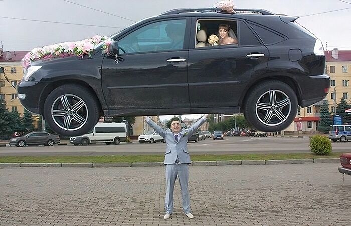 Man in a suit appears to lift a decorated wedding car with a bride inside in awkward wedding photos.