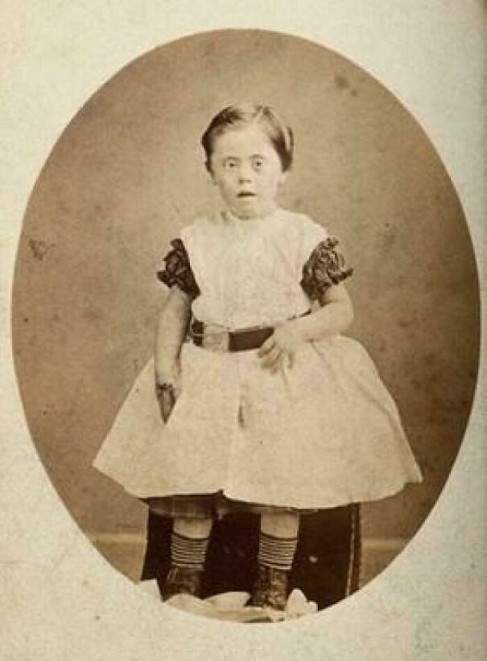 Victorian era sepia photograph of a young child in a dress and boots, showcasing fashion from a different time.