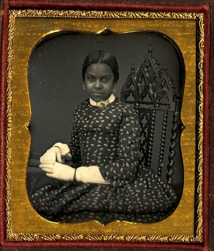 Victorian era portrait of a young woman in patterned dress sitting on an ornate wooden chair in an antique frame.