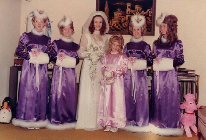 Bride and bridesmaids in mismatched outfits and unusual hairstyles posing in a vintage awkward wedding photo.