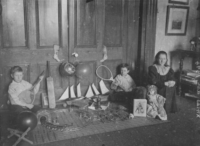 Victorian era children sitting indoors with vintage toys including balls, rackets, model boats, and dolls showing different times.