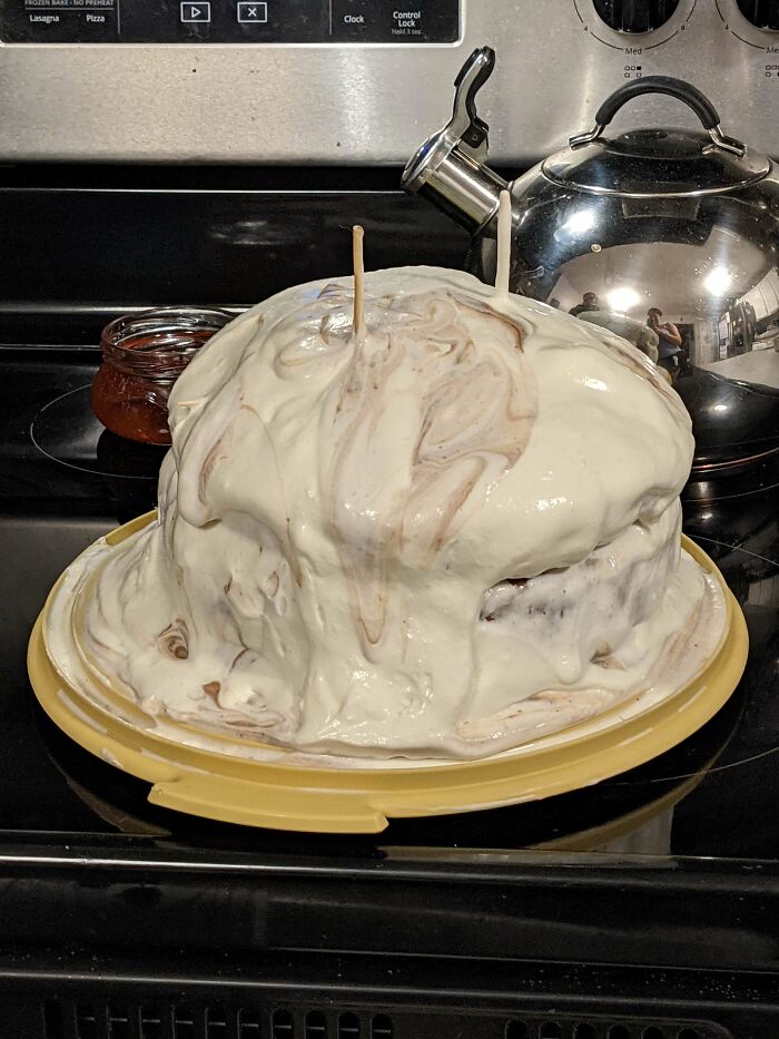 Cake covered with uneven, melted frosting resembling a failed dessert attempt on a kitchen stove.