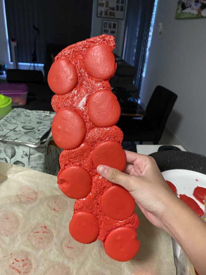 Hand holding a large misshapen cluster of red macarons baked together, illustrating dessert fails and ruined desserts.