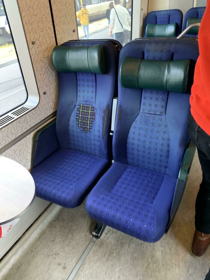 Worn down train seats showing fabric tear and discoloration from everyday use inside a passenger carriage.