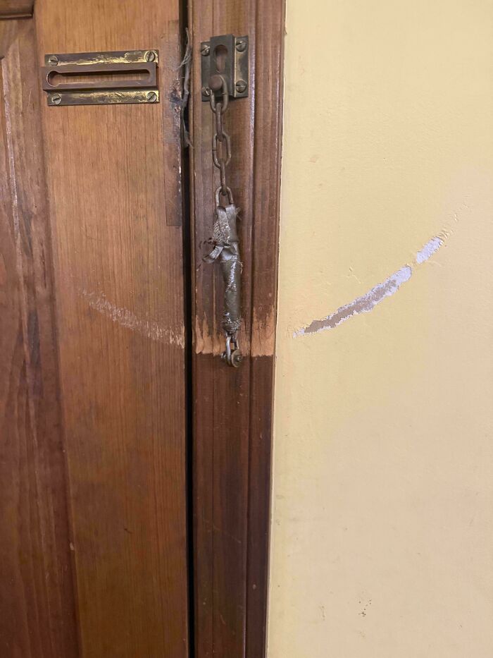 Worn down door frame and chain lock showing wear from everyday use with scratches on the adjacent wall.