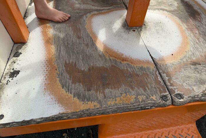 Worn wooden playground surface with faded paint and a child's foot, showing everyday objects worn down in unexpected ways.