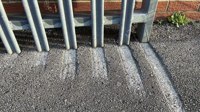 Worn down metal bike rack casting shadows on asphalt, showing signs of everyday objects worn in unexpected ways.