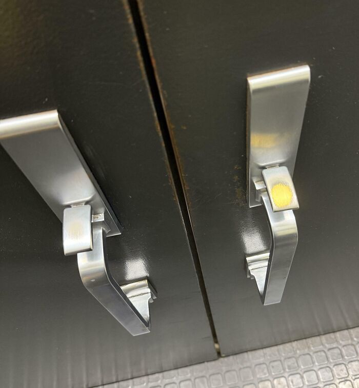 Worn down metal handles on black cabinet doors showing signs of everyday object wear and tear.