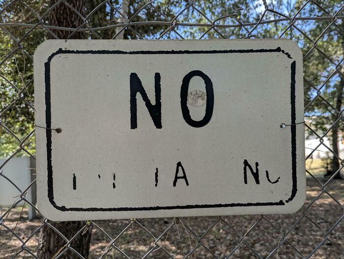 Worn down sign with faded letters on a chain-link fence showing everyday objects worn in unexpected ways.