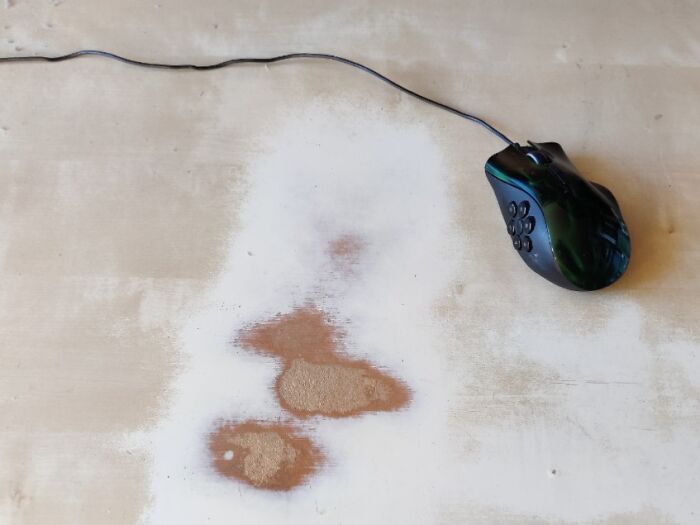 Worn down surface of a desk showing discoloration and scratches from an everyday object and a black computer mouse.