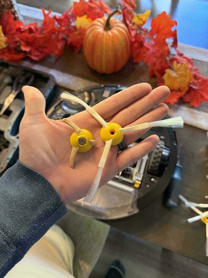 Worn down side brushes from a robot vacuum held in hand showing wear on bristles and yellow plastic parts.