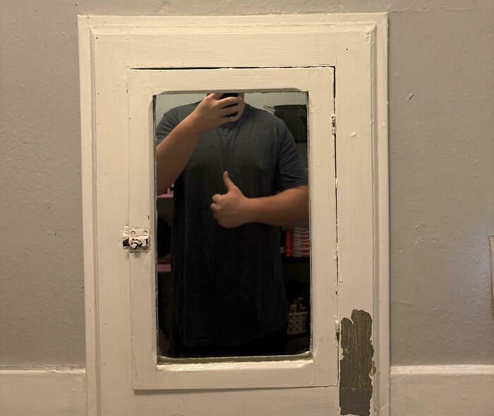 Person with a tall stature giving a thumbs up in a small mirror, highlighting struggles only tall people face.