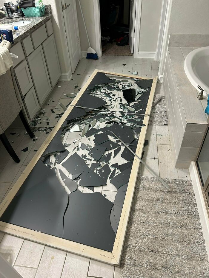 Broken large mirror shattered on bathroom floor showing an unfortunate and expensive fail inside a modern home.