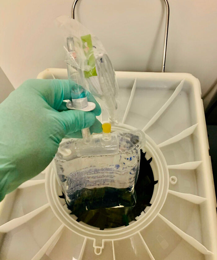 Hand in green glove holding a medical fluid bag above a large white container, illustrating expensive fails in healthcare equipment.