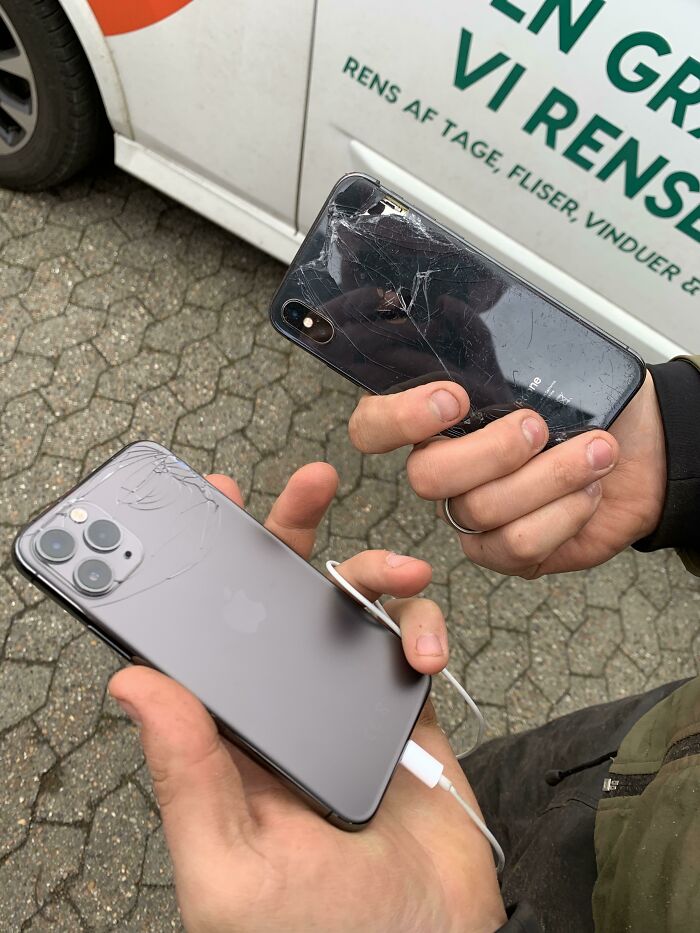 Two hands holding c*****d iPhones showing unfortunate and expensive phone screen fails outdoors near a vehicle.