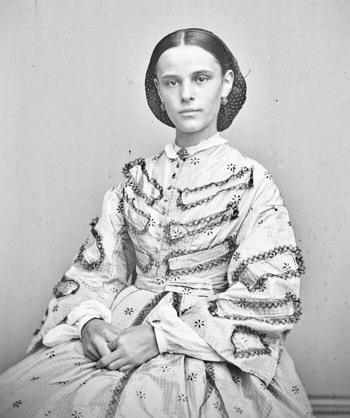 Victorian era woman in detailed period dress sitting with hands folded, showcasing fashion from the different Victorian era time.
