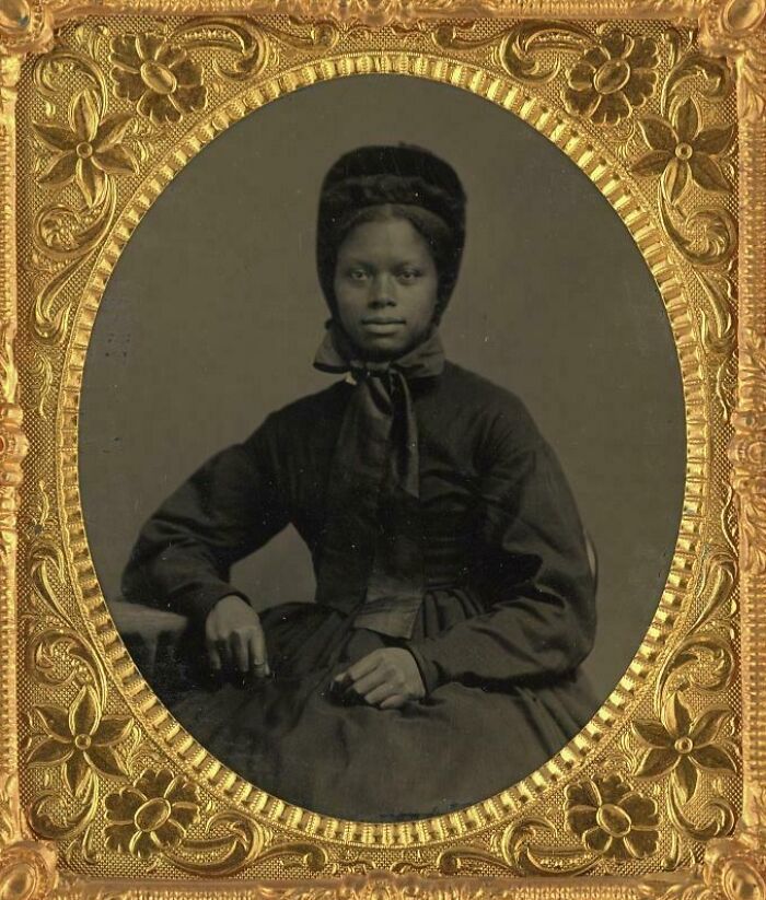 Victorian era portrait of a woman wearing a dark dress and bonnet, framed in an ornate gold floral frame.