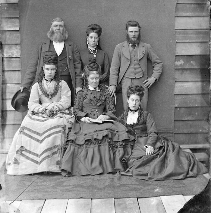 Group portrait of six Victorian era people in period clothing, showcasing fashion and style from the Victorian era.